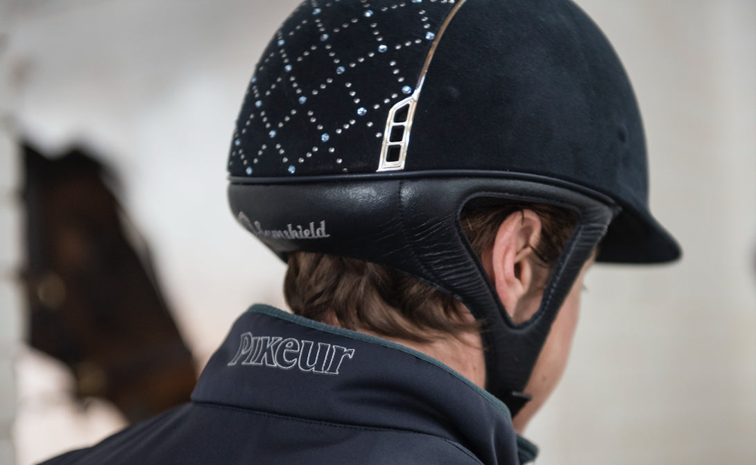 The head of a person wearing a riding helmet, from behind
