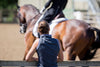 Taken from behind, a woman watching a horse being ridden in an outdoor ring