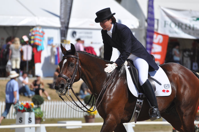 Woman in dress riding gear riding a horse during a competition