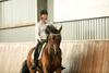 Woman riding a brown horse in an indoor riding ring