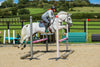 Side view of a white horse being ridden over a jump