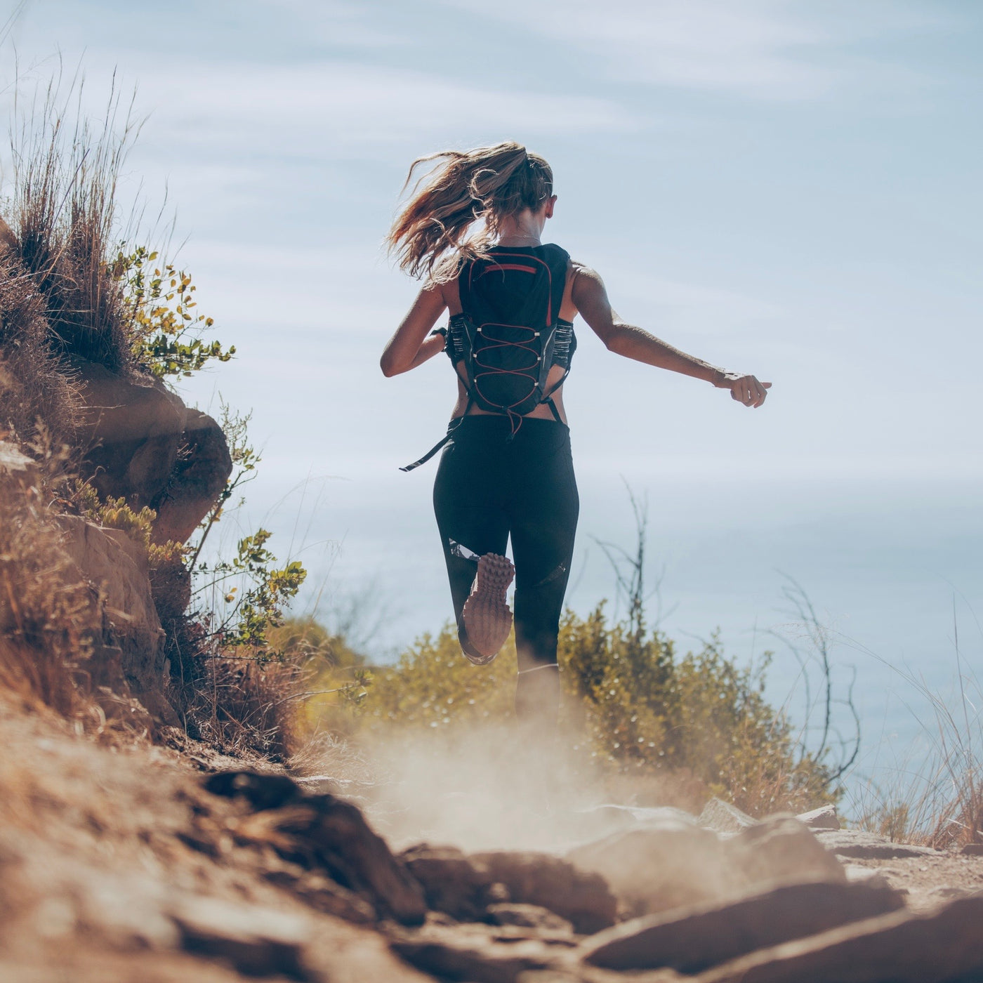 The back of a woman while she runs along some cliffs